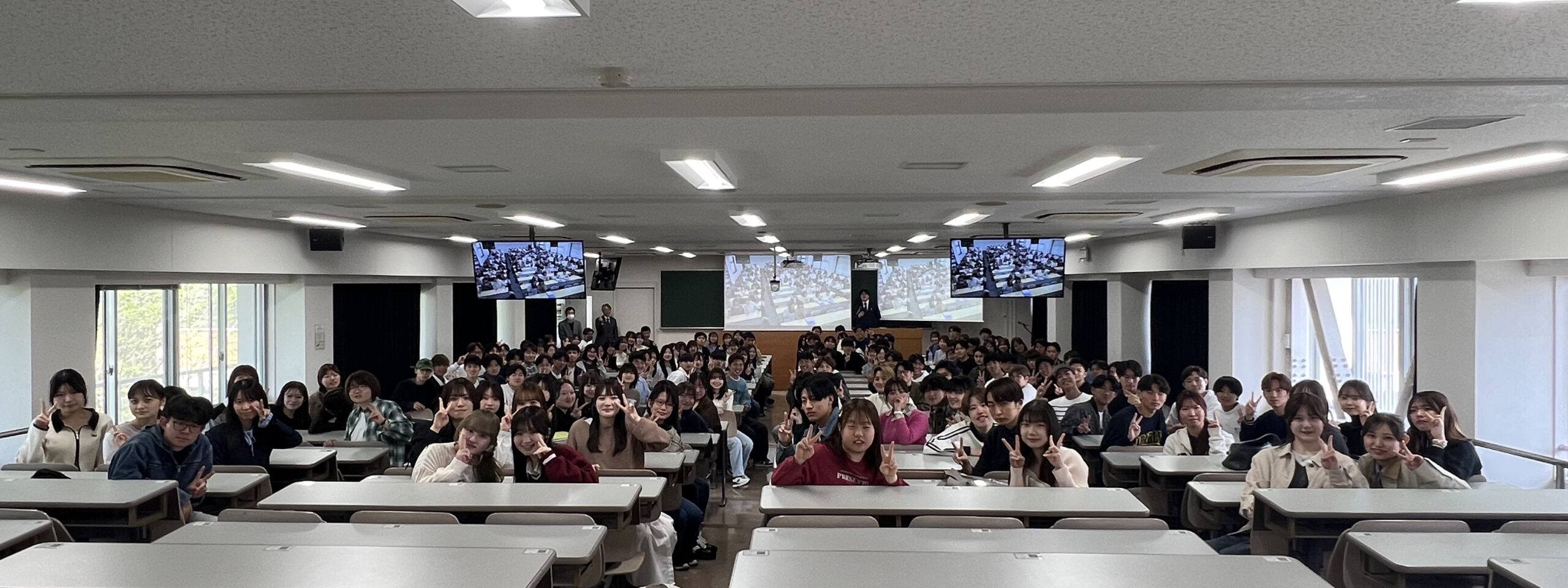 スクリーンに映る佐賀大学の学生たちと共に記念撮影をする熊本大学の学生たち